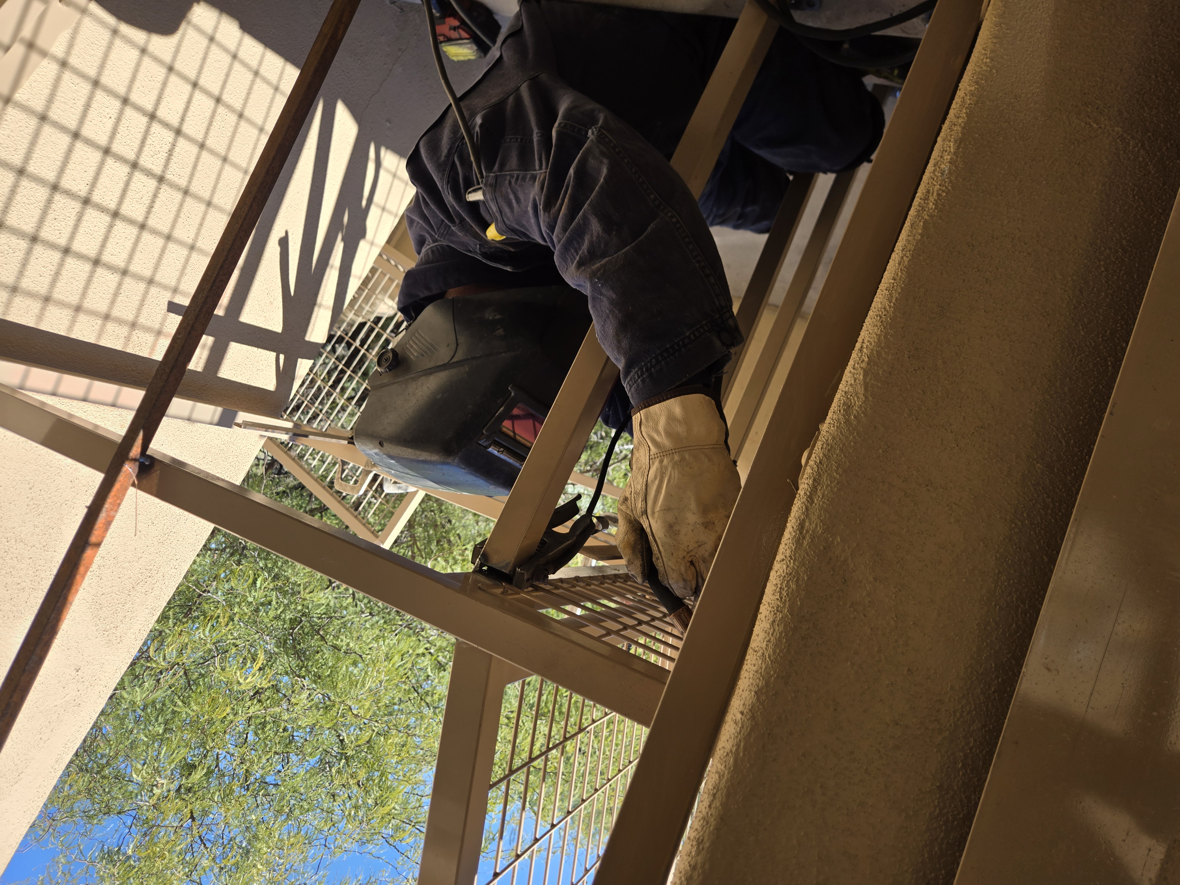 Welder under the structure making overhead welds on the roof supports